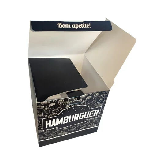 Caixa hambúrguer personalizada na cor preta, com uma textura de fundo branca com vários desenhos de sanduíches, cachorro-quentes, refrigerantes e batatas. Na parte da frente é possível ver palavra "hambúrguer" dentro da silhueta de um hambúrguer. A embalagem está aberta e na lingueta que fecha a caixa está escrito "Bom apetite", a orelha esquerda da embalagem está fechada e a direita está aberta.