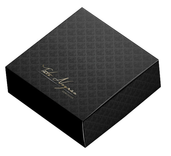 Uma caixa cinza chumbo com arabescos pretos, ela se assemelha a uma caixa de fósforos e tem um logotipo escrito a mão em dourado "Tati Negrão Semijoias"