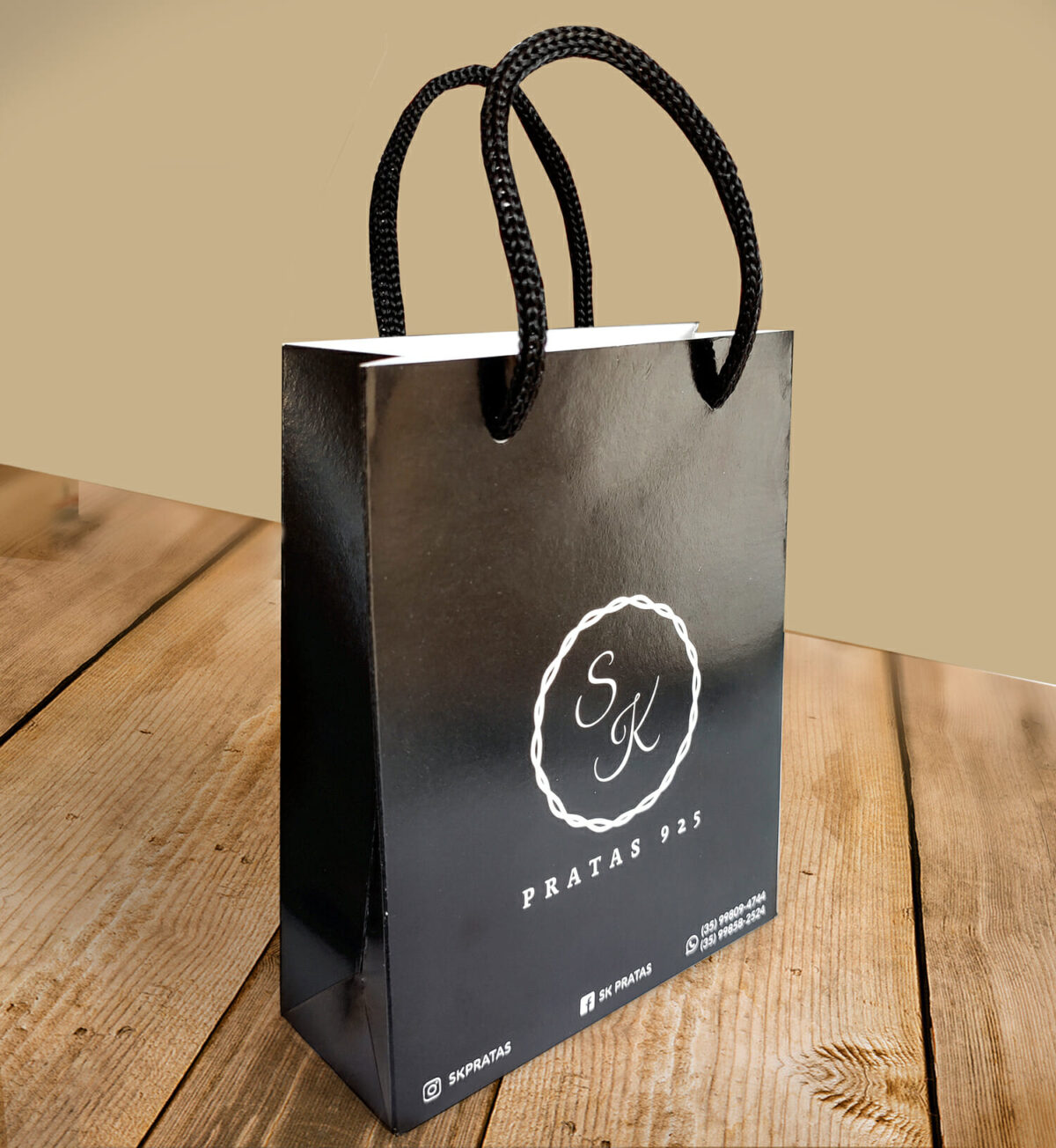 Mini Sacola Personalizada na cor preta com o logo da empresa SK Semi joias. Está sobre uma mesa.