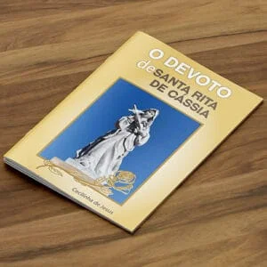 Livro com lombada canoa e grampo. Vemos um livro com pouco páginas, capa colorida predominantemente amarela com a imagem de Santa Rita de Cássia com título 