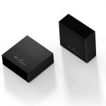 Duas caixas cinza chumbo com arabescos pretos, ela se assemelha a uma caixa de fósforos e tem um logotipo escrito a mão em dourado 