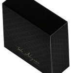 Uma caixa cinza chumbo com arabescos pretos, ela se assemelha a uma caixa de fósforos e tem um logotipo escrito a mão em dourado 
